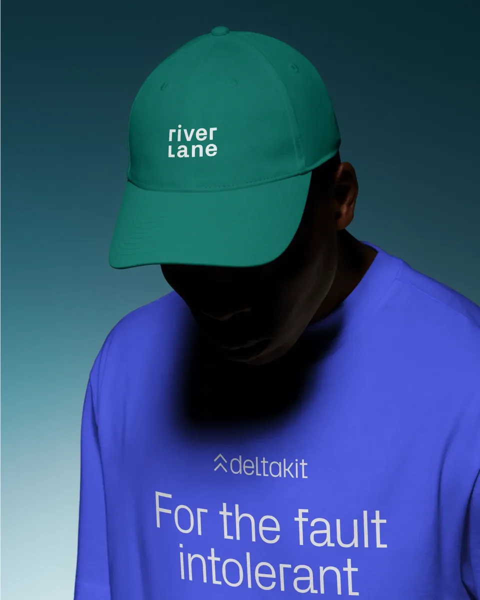 Person wearing a green Riverlane cap and a blue Deltakit T-shirt with the slogan ‘For the fault intolerant’ against a gradient background.
