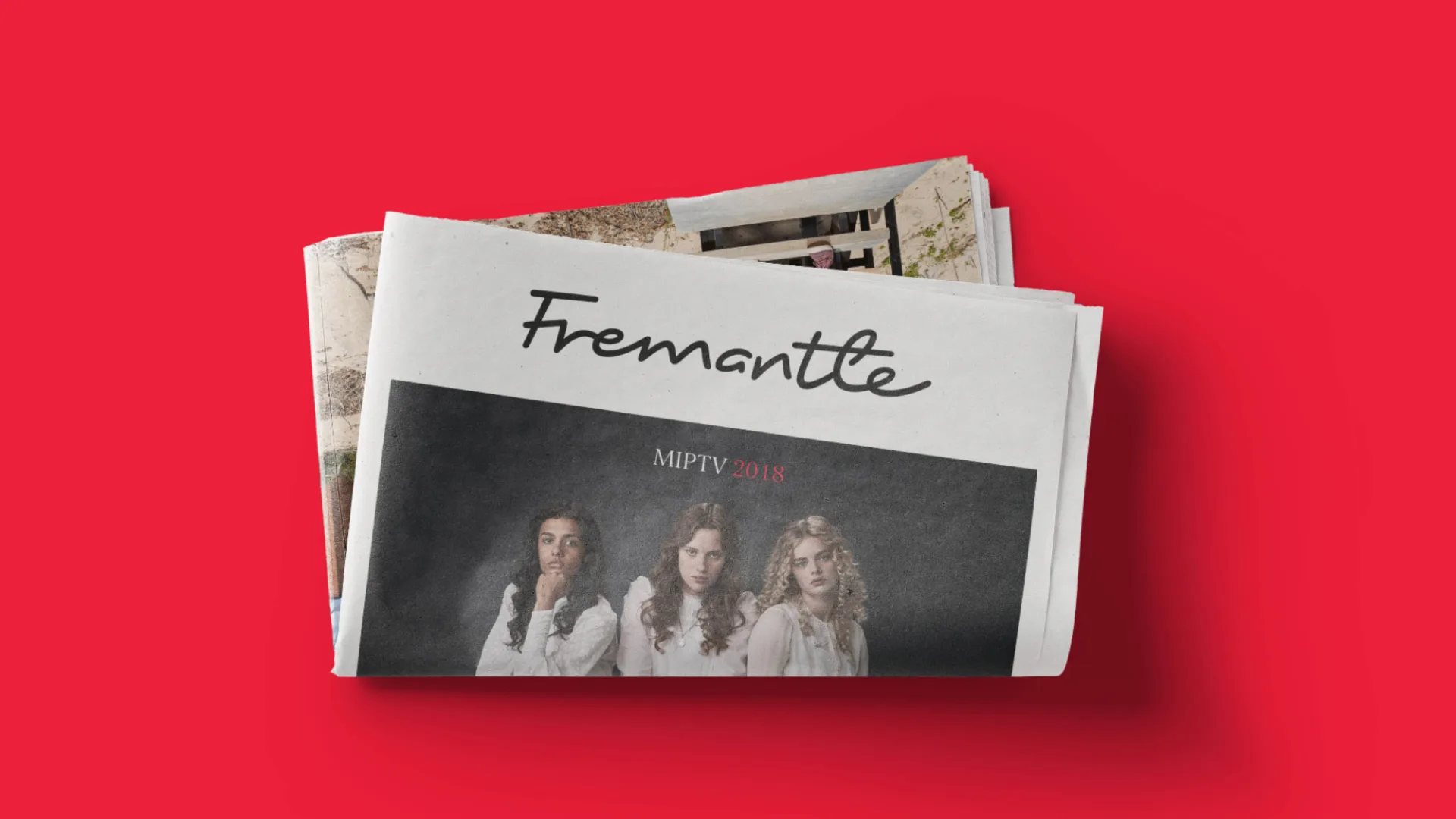 Newspaper featuring a photo of 3 women with the name Fremantle, sat folded on a red background.